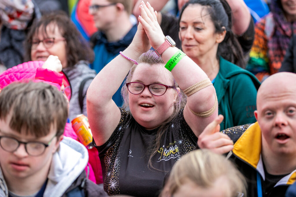 A young woman clapping, with her hands up, in the crowd at Ablefest