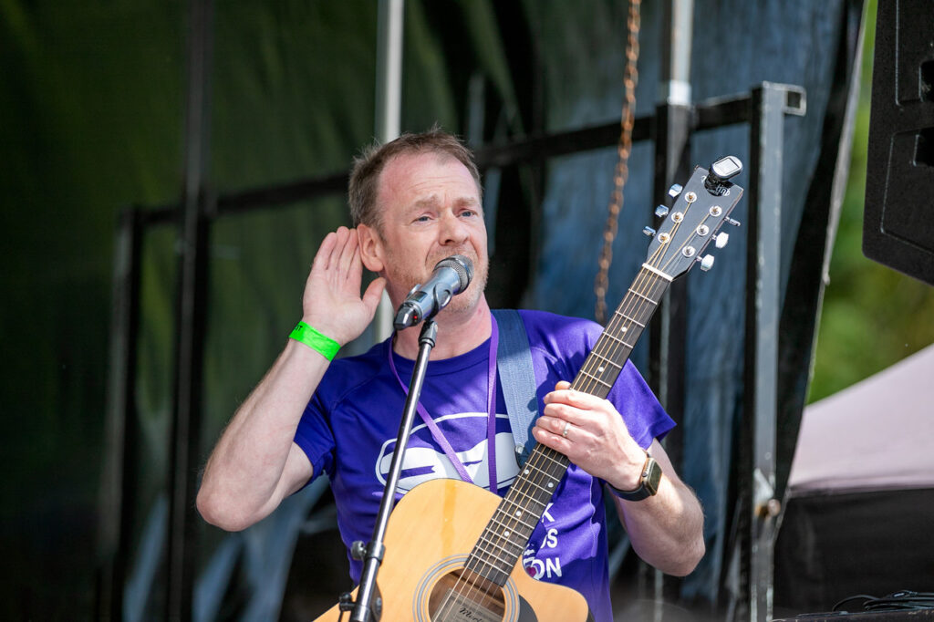 Artist holding a guitar and performing on stage at the fully inclusive festival Ablefest