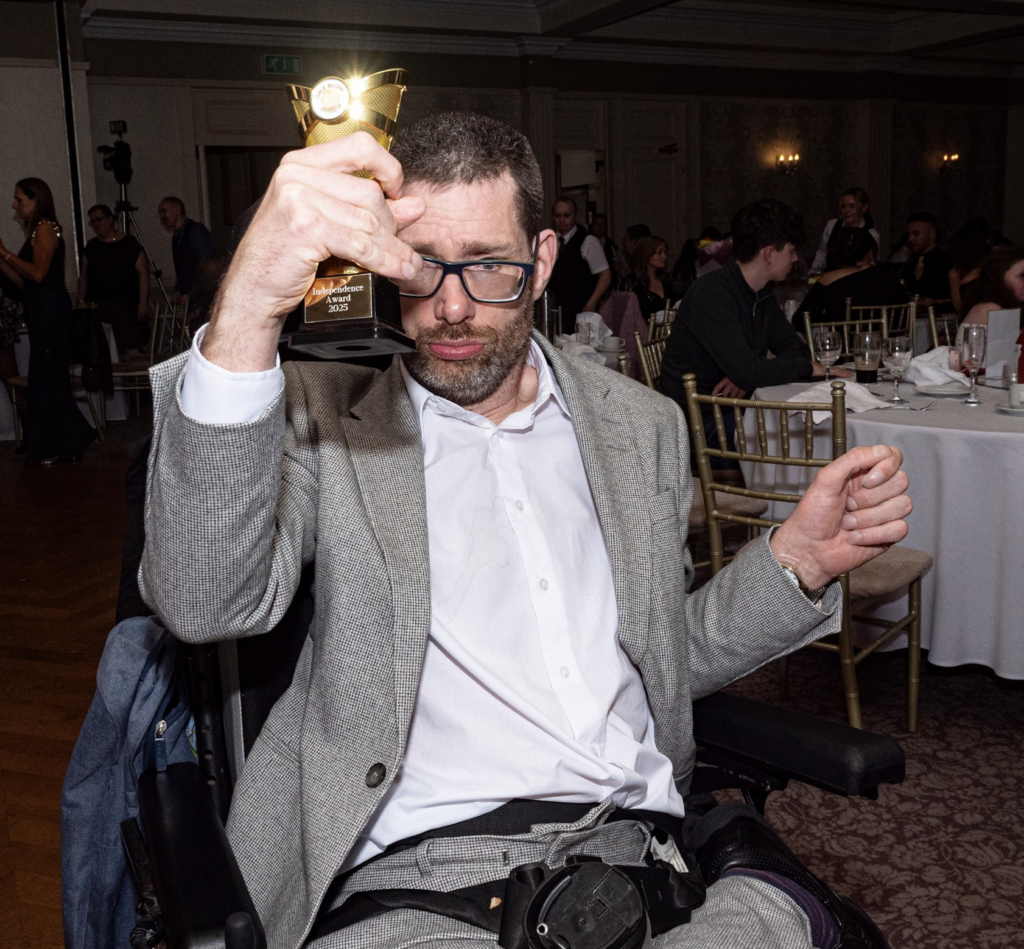 Photo of a man in a wheelchair happily holding a trophy in one hand at an Able Events celebration