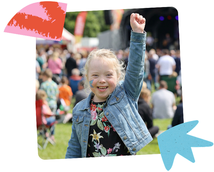Photo of a young girl smiling at Ablefest. Behind her is the crowd and the main stage of the inclusive event.
